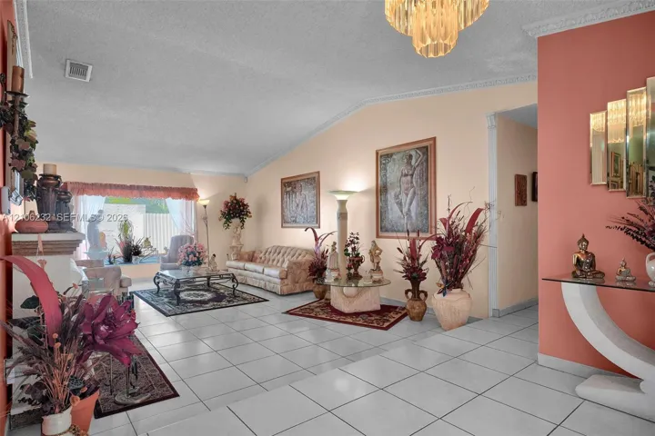 Vaulted ceiling with decorative crown molding and an integrated chandelier, complemented by neutral tile flooring