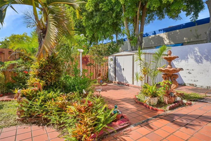 Terracotta tile patio featuring a tiered stone fountain, mature landscaping, and an enclosed storage structure surrounded by wood fencing