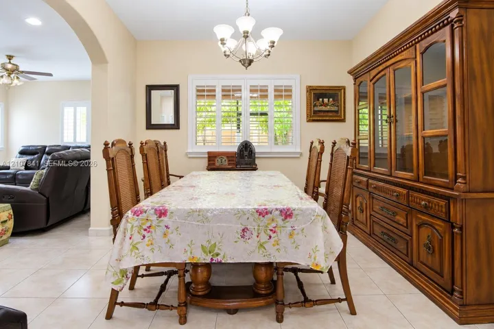 Dining area featuring tile flooring, arched entry, custom window shutters, and a central multi-light chandelier