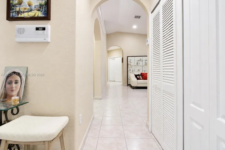 Hallway featuring arched architectural openings, neutral ceramic tile flooring, and white louvered-style closet doors