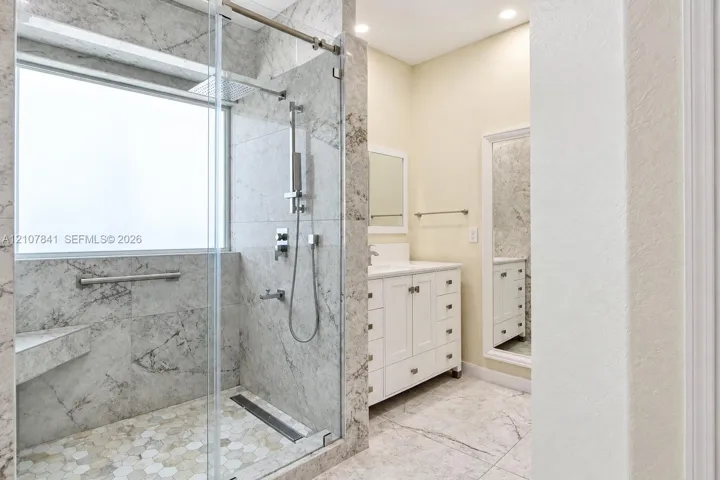 Walk-in shower featuring full-height natural stone tiling, a glass enclosure, a rainfall showerhead, and a built-in bench, accompanied by a white vanity with integrated cabinetry
