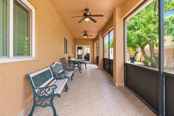 Screened-in lanai featuring tile flooring, dual ceiling fans, stucco exterior walls, and a multi-pane glass entry door
