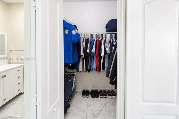 Walk-in closet featuring wire shelving, white cabinetry, and stone-finish flooring