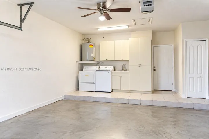 Garage area featuring a concrete floor, tile-surfaced elevated workspace, built-in cabinetry with integrated sink, ceiling fan, and laundry hookups
