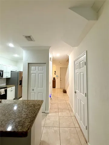 Neutral-toned floor tiling, kitchen island with stone-finish countertop, white six-panel interior doors, and recessed lighting