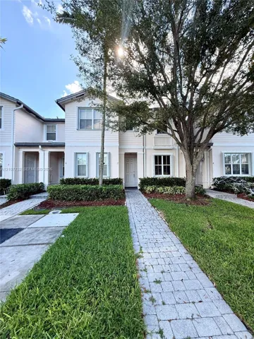 Two-story exterior featuring lap siding, multi-pane windows, a paved walkway, manicured hedging, and mature landscaping