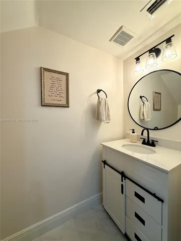 White vanity with sliding barn-door style cabinetry, matte black hardware, stone-composite countertop, oval wall-mounted mirror, and industrial-style three-light fixture