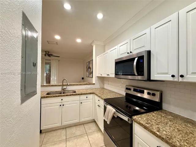 Kitchen featuring white shaker-style cabinetry, speckled stone-finish countertops, subway tile backsplash, stainless steel microwave, and dual-basin stainless steel sink