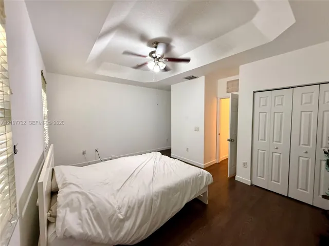 Tray ceiling featuring a central light fixture and fan, wood-finish flooring, and multi-panel bi-fold closet doors