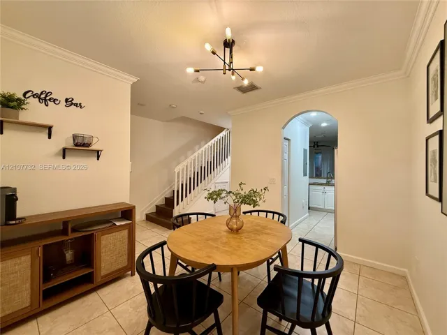 Dining area featuring ceramic tile flooring, crown molding, a multi-arm modern light fixture, and an arched entryway leading to the kitchen