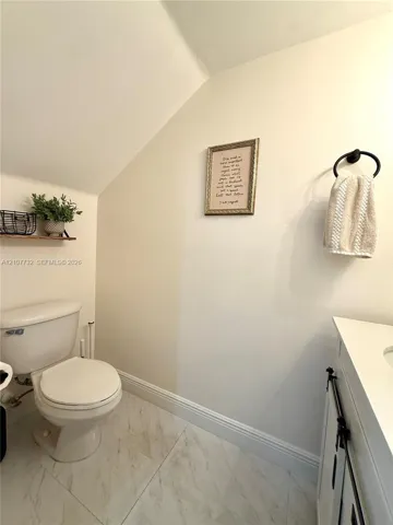 White vanity with integrated basin, light-toned stone-finish tile flooring, and wall-mounted towel ring
