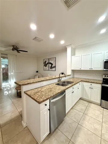 Kitchen featuring white cabinetry, stone-surface countertops, stainless steel appliances, dual-basin sink, and ceramic tile flooring