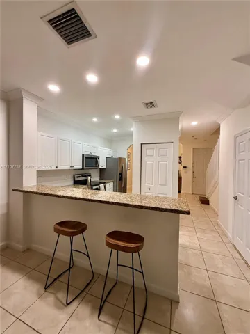 Kitchen featuring a stone-look countertop breakfast bar, white cabinetry, recessed lighting, and tile flooring