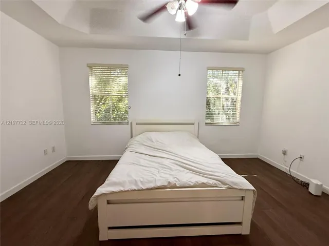 Tray ceiling featuring a central multi-light ceiling fan, dual windows with horizontal blinds, and wood-finish flooring