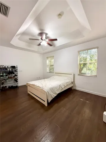 Tray ceiling featuring a central ceiling fan with integrated lighting and wood-finish flooring throughout