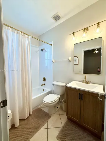 Bathroom featuring a wood-finish vanity with a rectangular sink, brass-tone hardware, a wall-mounted rectangular mirror, and a tiled tub-shower combination