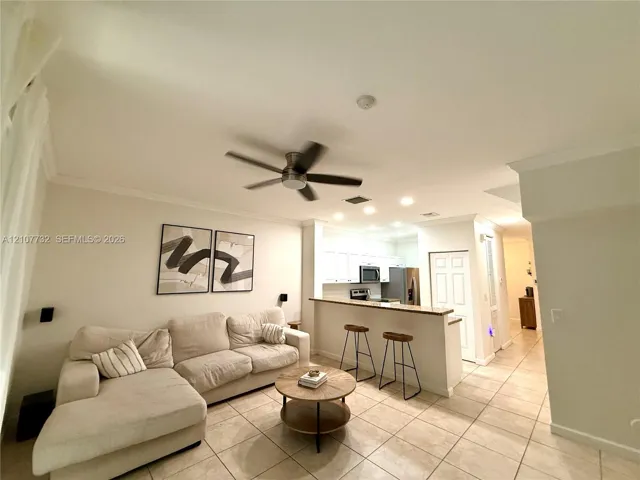 Open concept interior featuring tile flooring, crown molding, ceiling fan, and kitchen breakfast bar with stone-surfaced countertop