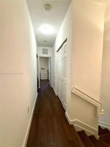Hallway featuring wood-finish flooring, white paneled bi-fold closet doors, and a staircase with a white handrail