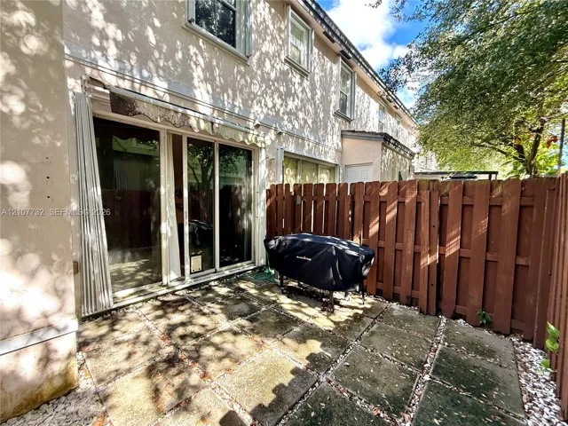 Stucco exterior with sliding glass patio doors, stone-paver patio, and wood privacy fencing