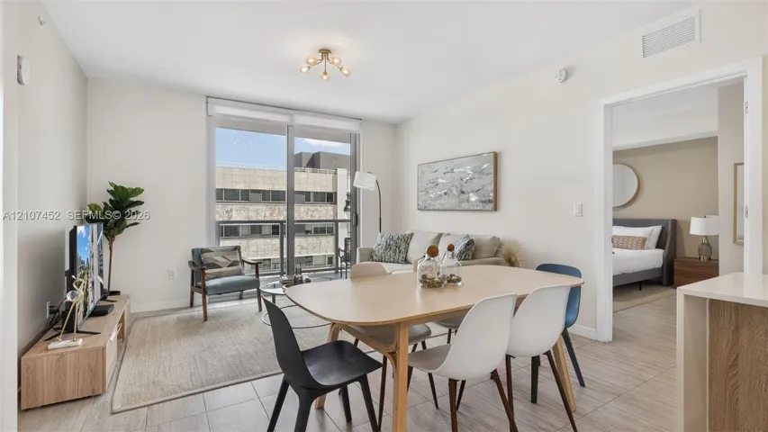 Open-concept interior featuring large-format ceramic tile flooring, neutral wall tones, multi-light flush-mount ceiling fixture, and full-height sliding glass doors leading to a private balcony