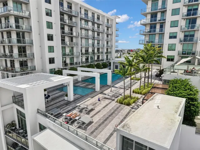 Swimming pool terrace featuring large-format paver tile decking, pergola structures, integrated landscaping, and glass-paneled balconies
