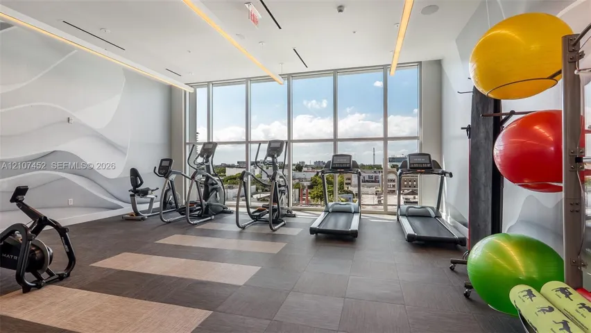 Fitness center featuring floor-to-ceiling windows, sculptural wall molding, recessed linear lighting, and large-format tile flooring