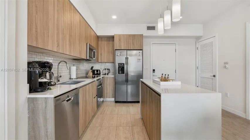 Kitchen featuring wood-finish cabinetry, stone-style countertops, stainless steel appliances, subway tile backsplash, and a central island with pendant lighting
