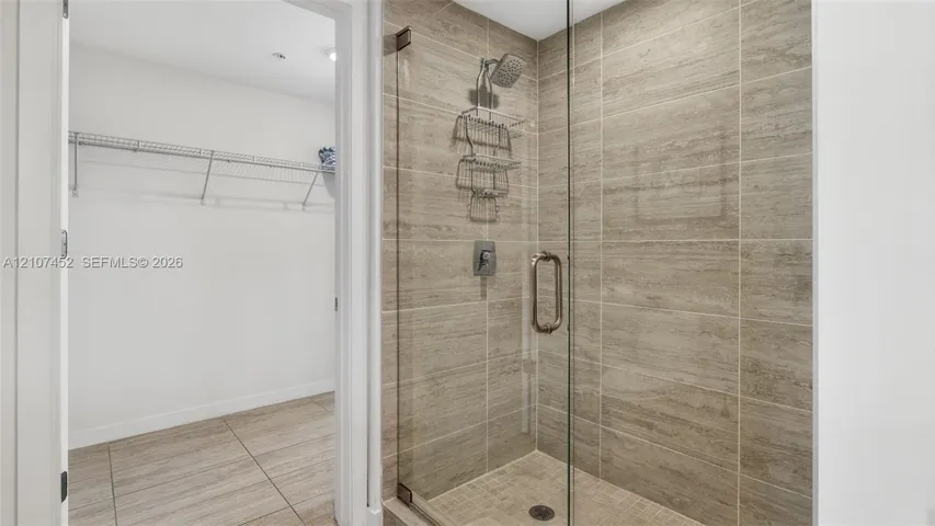 Walk-in shower featuring glass door enclosure, neutral-toned tiled walls, and metallic hardware, paired with a walk-in storage space with wire shelving