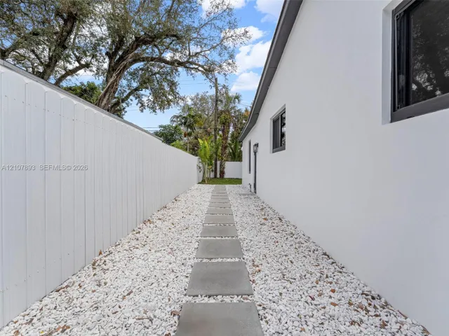 Side yard featuring a concrete paver walkway, white rock ground cover, and a solid white privacy fence