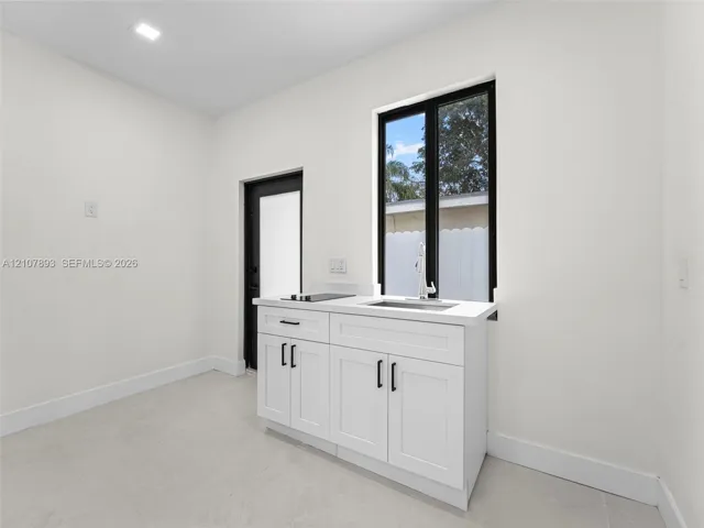 Shaker-style white cabinetry with matte black hardware, stone-finish countertop, integrated stainless steel sink, and recessed ceiling lighting