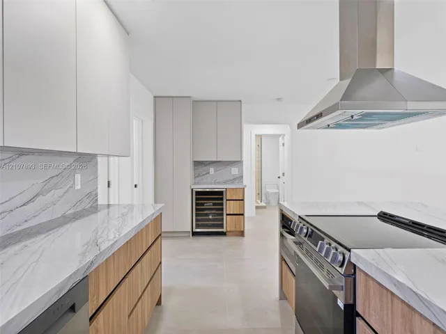 Kitchen featuring flat-panel wood and matte-finish cabinetry, stone-surface countertops with continuous backsplash, built-in wine refrigeration, stainless steel professional-style range, and wall-mounted stainless steel vent hood