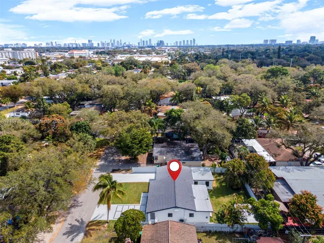 Aerial perspective featuring a detached residential property with a shingle roof, paved driveway, landscaped grounds with mature trees, and a perimeter fence