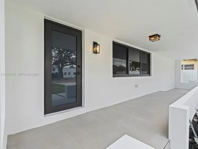 Covered entryway featuring large-format tile flooring, a full-glass entry door with dark trim, dual wall-mounted lanterns, and a flush-mount ceiling fixture