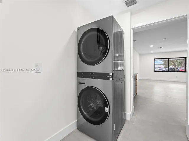 Stainless steel stacked laundry unit featuring front-loading washer and dryer with integrated digital controls and large-format tile flooring