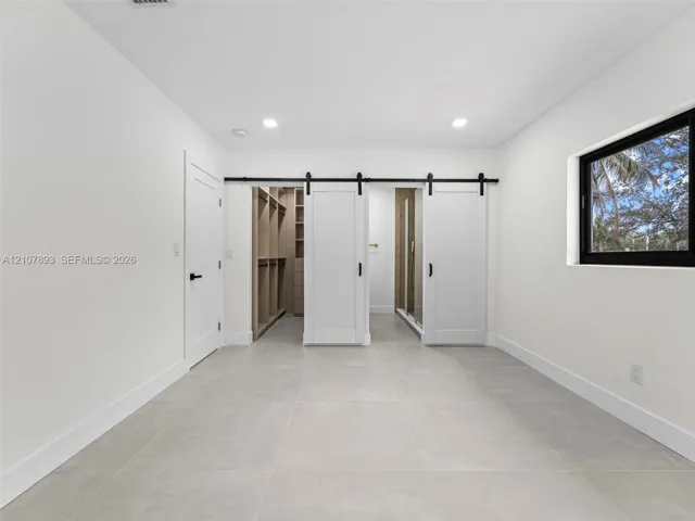 Large-format tile flooring, dual sliding barn-style doors with matte black hardware, built-in closet storage system, and recessed lighting