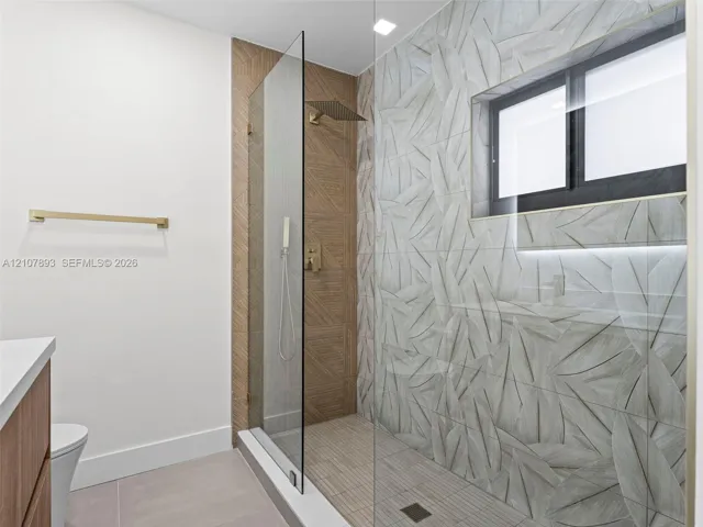 Walk-in shower featuring gold-tone rainfall and handheld showerheads, glass enclosure, leaf-patterned wall tile, and built-in niche lighting