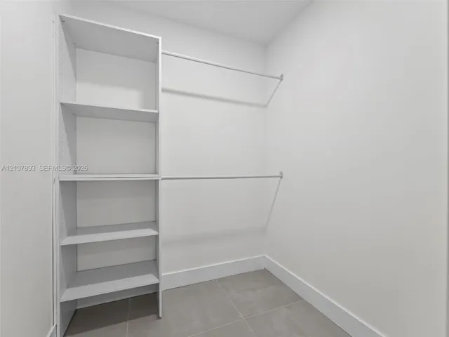 Walk-in closet featuring white built-in shelving and dual-tier metal hanging rods with neutral tile flooring