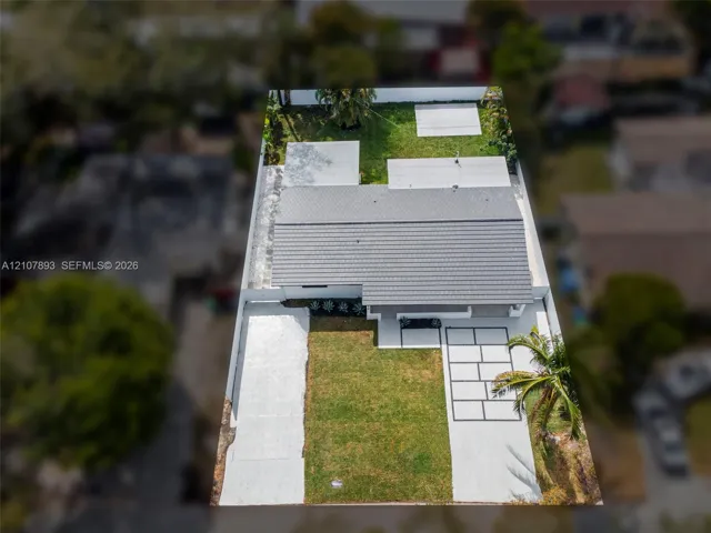 Aerial view of property featuring a concrete tile roof, paver driveway, concrete parking pad, manicured lawn, and perimeter privacy fencing