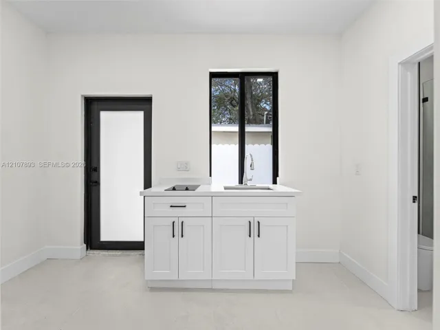Kitchenette featuring white shaker-style cabinetry, a light-toned countertop, a stainless steel sink with a high-arch faucet, a built-in two-burner induction cooktop, and contrasting black window and door frames