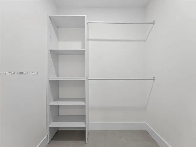 Walk-in closet featuring white built-in shelving and dual horizontal hanging rods over tile flooring