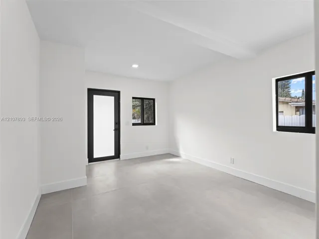 Neutral interior space featuring large-format tile flooring, matte black window and door frames, and flush-mount recessed lighting