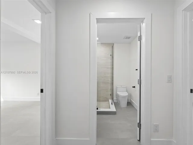 Bathroom featuring a glass-enclosed shower with large-format wall tile, a two-piece toilet, and grey tile flooring