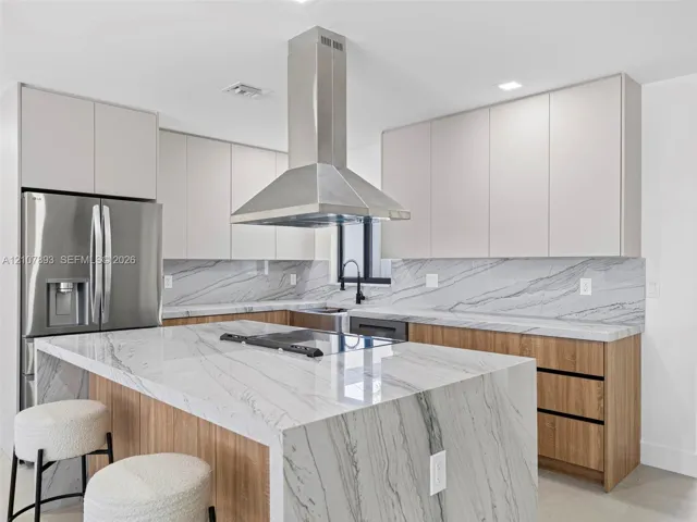 Kitchen featuring waterfall-edge stone countertops, stainless steel chimney-style range hood, dual-tone cabinetry, and wood-finish lower cabinetry
