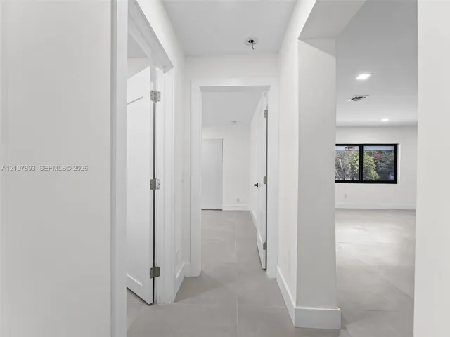 Neutral-toned large-format tile flooring, crisp white walls, recessed ceiling lighting, and black-trimmed window frames