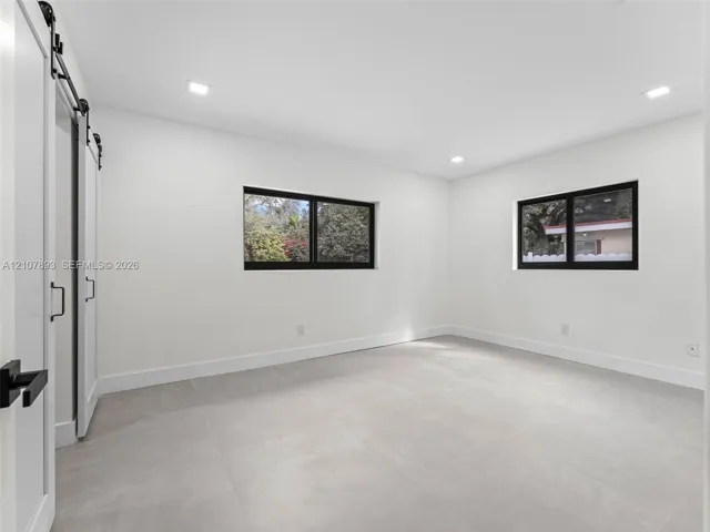 Interior space featuring neutral large-format tile flooring, recessed lighting, dual-pane windows with black frames, and a white sliding barn door with matte black hardware