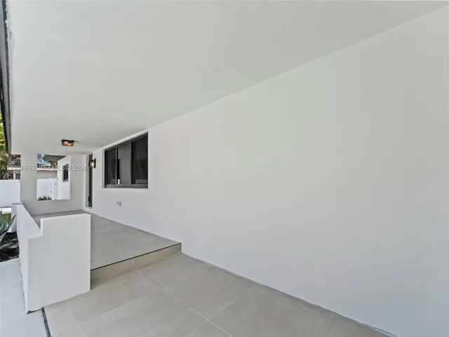 Covered porch featuring large-format tile flooring, a solid masonry partition wall, and wall-mounted exterior lighting fixtures