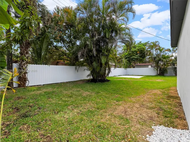 Backyard featuring a grass lawn, white vinyl fencing, mature landscaping, and a concrete patio slab