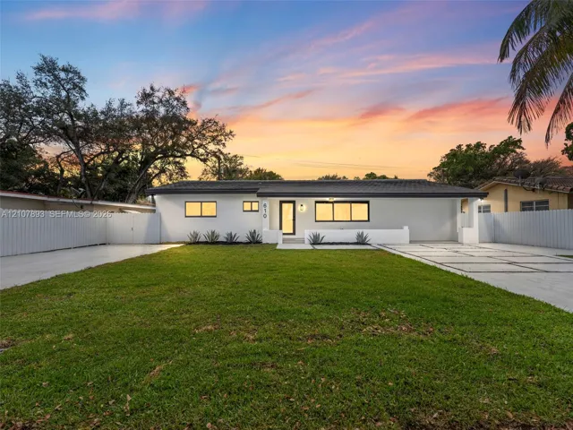 Single-story residence featuring a smooth stucco exterior, low-pitch roofline, paver driveway with decorative grass inlays, manicured lawn, and perimeter privacy fencing