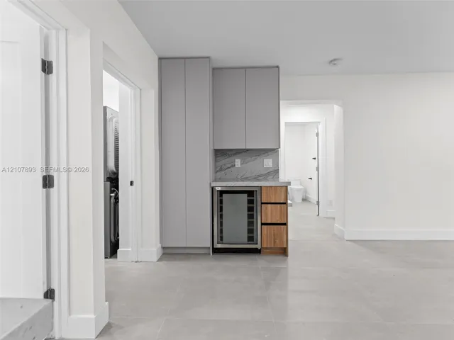 Built-in cabinetry featuring grey slab-front doors, integrated wine refrigerator, wood-finish drawers, and stone-finish backsplash