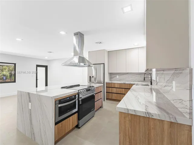 Kitchen featuring waterfall-edge stone countertops, wood-finish cabinetry, stainless steel range and built-in microwave, stainless steel chimney-style range hood, and tile flooring